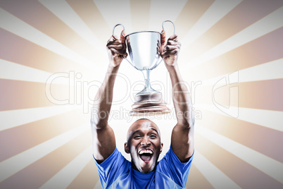 Composite image of happy athlete cheering while holding trophy