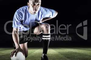 Composite image of serious rugby player kneeling while holding b