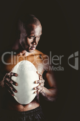 Concentrated shirtless athlete with rugby ball