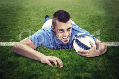 Composite image of confident rugby player lying in front with ba