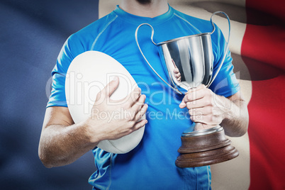 Composite image of rugby player holding trophy and ball