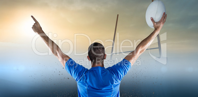 Composite image of rear view of rugby player holding ball with arms raised
