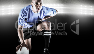 Composite image of serious rugby player kneeling while holding b