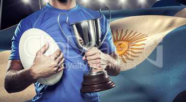 Composite image of rugby player holding trophy and ball