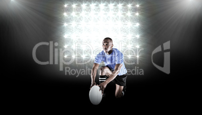 Composite image of rugby player holding ball while kneeling