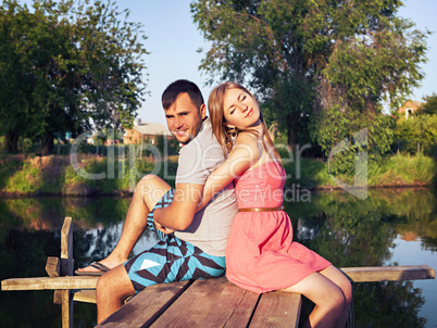 young couple sitting embracing on the bridge by the river