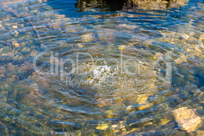 Water bubbling in pond with green rocks