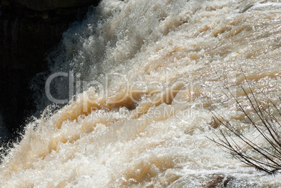 Rushing muddy waterfall rapids with branch