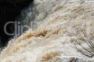 Rushing muddy waterfall rapids with branch