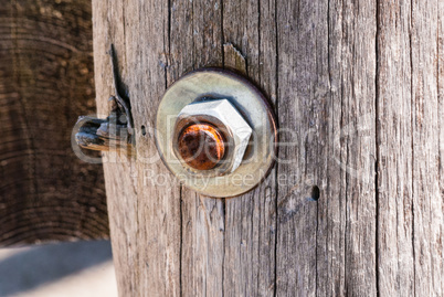 Rusted metal screw with nut in wood post