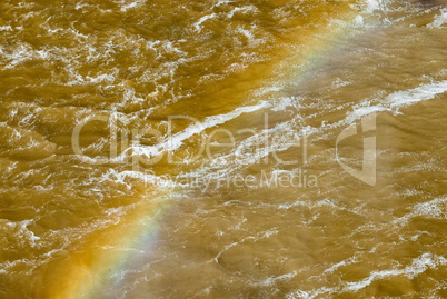 Vivid rainbow across churning muddy river