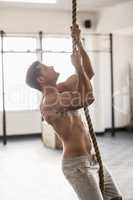 Side view of muscular man doing rope climbing