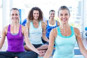 Women smiling while doing easy pose in fitness studio