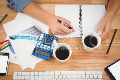 Hipster holding coffee while writing on spiral notebook