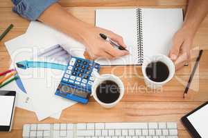Hipster holding coffee while writing on spiral notebook