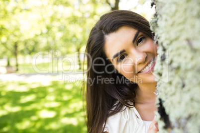 Portrait of smiling woman behind tree trunk