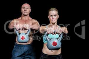 Portrait of muscular man and woman lifting kettlebells