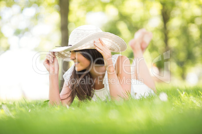 Happy young woman holding sun hat while lying on grassland