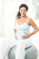 Happy pregnant woman touching her belly while sitting on exercis