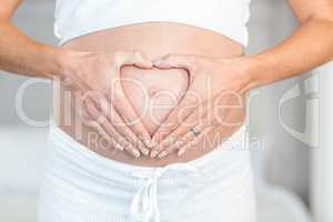 Midsection of woman making heart on belly