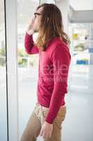 Hipster talking on mobile phone while standing by window