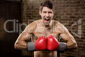 Shirtless man smiling while wearing boxing gloves