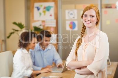 Businesswoman standing with arms crossed while colleagues workin