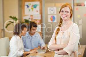 Businesswoman standing with arms crossed while colleagues workin