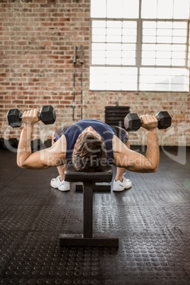 Man doing exercise with dumbbells while lying on bench