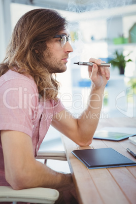 Hipster smoking electronic cigarette at desk in office