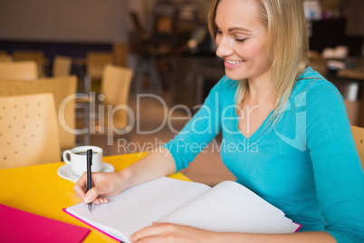 Young woman smiling while writing on book Young woman smiling while writing on book