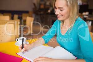 Young woman smiling while writing on book
