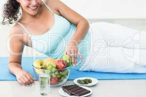 Smiling pregnant woman lying by fruits and chocolates