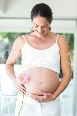 Happy woman holding flower by belly