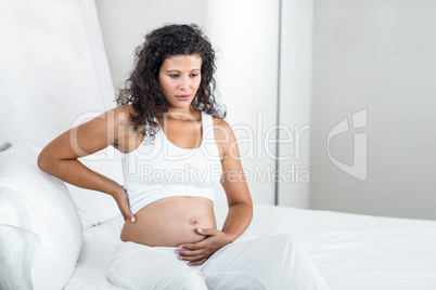 Pregnant woman touching tummy while sitting on bed