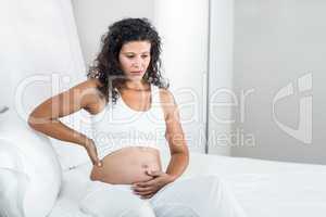 Pregnant woman touching tummy while sitting on bed