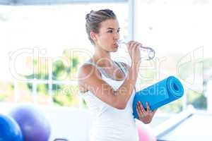 Beautiful woman drinking water while holding yoga mat