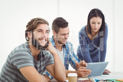 Smiling man looking away with coworkers using digital tablet