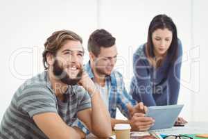 Smiling man looking away with coworkers using digital tablet