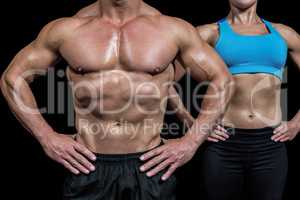 Midsection of muscular man and woman standing with hands on hip