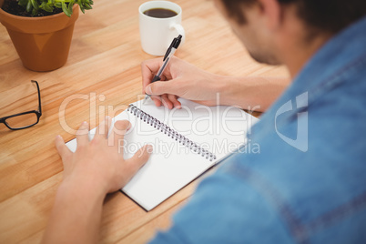 Hipster writing on spiral book at desk