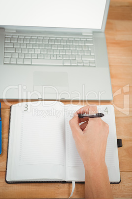 Man writing in diary while laptop at desk in office