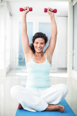 Pregnant woman lifting dumbbells while sitting on exercise mat