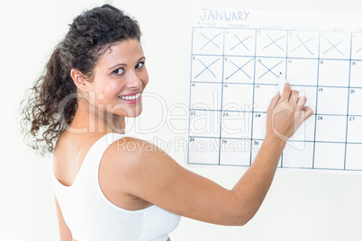 Happy pregnant woman marking off dates on calendar