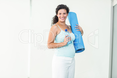 Smiling pregnant woman holding exercise mat and water bottle