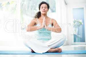 Pregnant woman sitting on exercise mat with hands joined