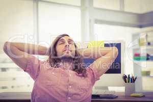 Hipster with hands behind head resting at computer desk