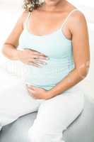 Pregnant woman sitting on exercise ball holding her belly