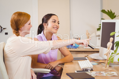 Businesswoman showing something on computer to female colleague