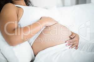 Pregnant woman embracing her belly while resting in bed